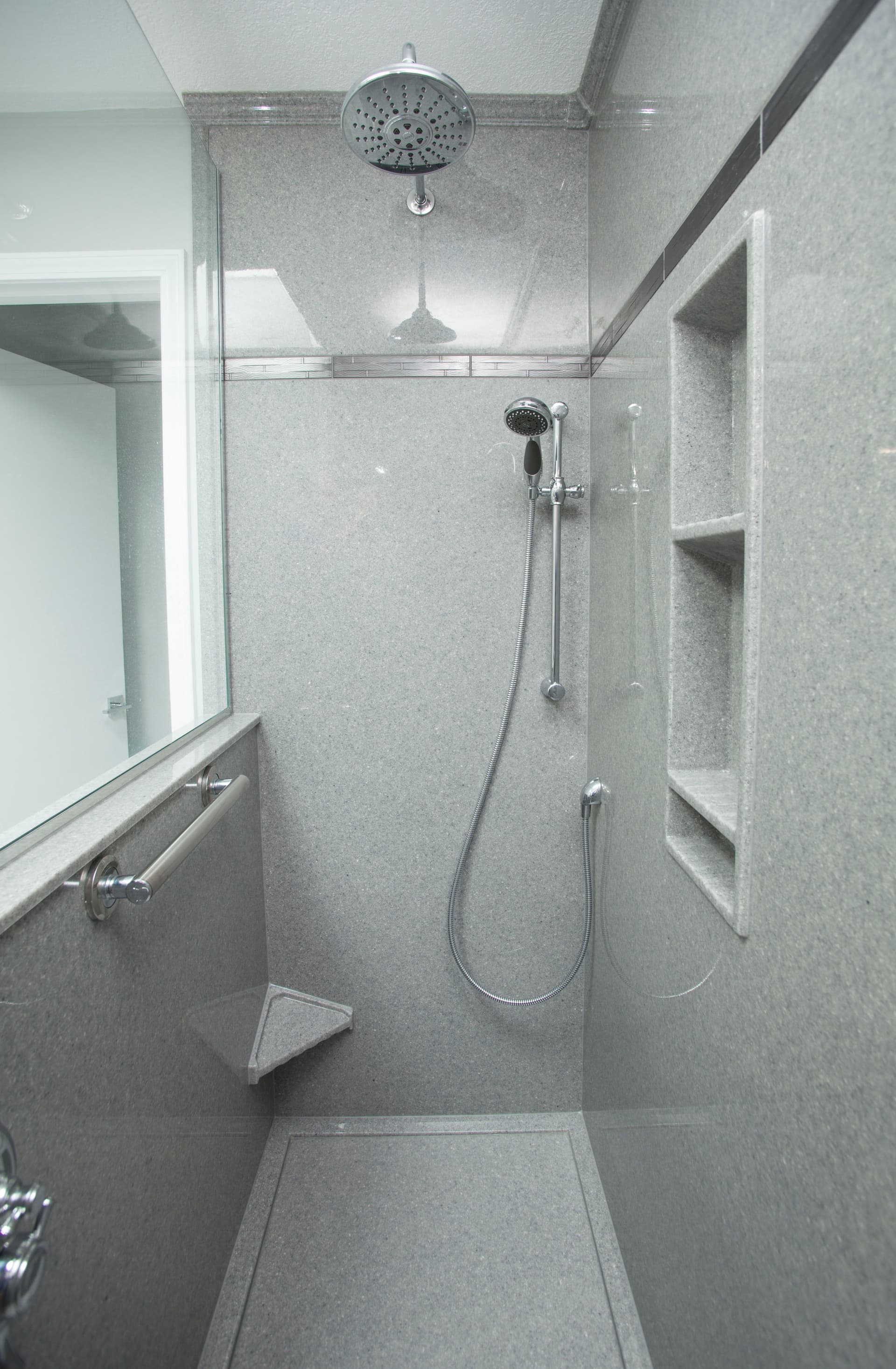 Walk-in shower with a rainfall head, handheld shower wand, vertical grab bar, built-in shelving, and a corner seat.